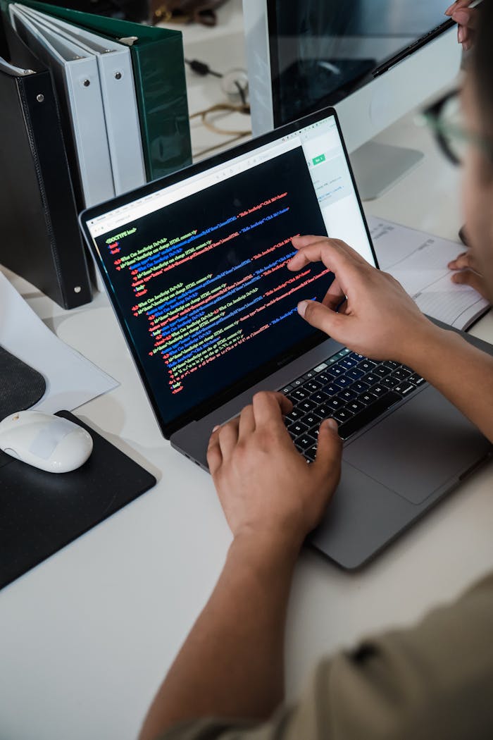 service-04 Close-up of a programmer pointing at a colorful code script on a laptop in an office setting.