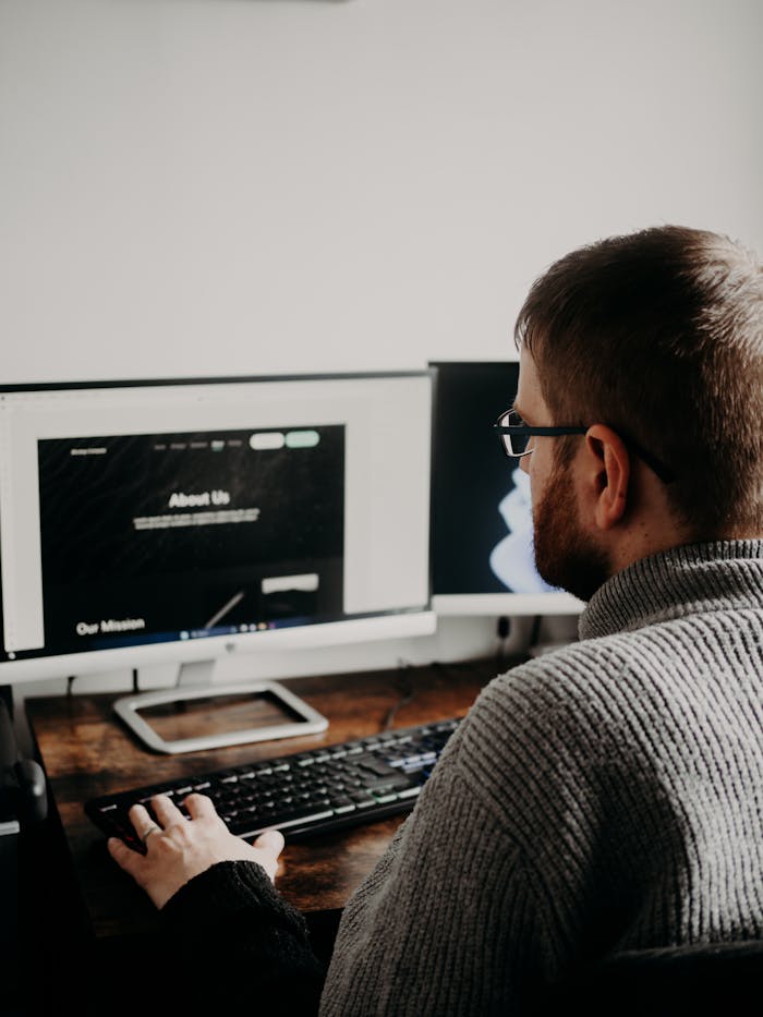 who-we-are Man working on web design at home office setup with dual monitors.